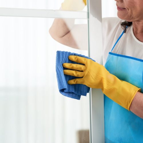 cropped-woman-cleaning-window-wearing-special-apron-min